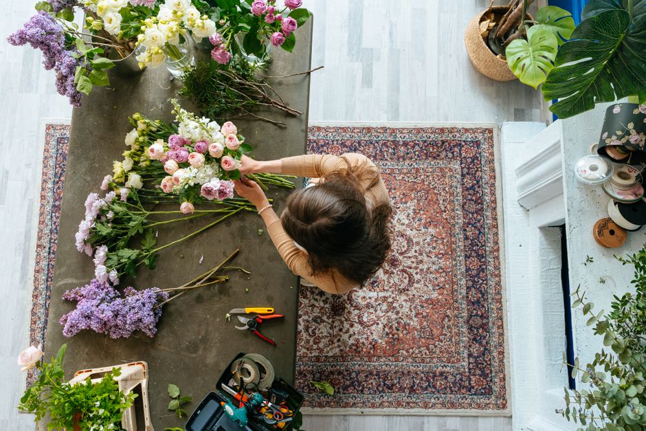 A top florist near New Malden Station arranging a bouquet of fresh flowers on a dark wooden table, featuring light pink roses, purple lilacs, and white flowers. The florist, viewed from above, is usin